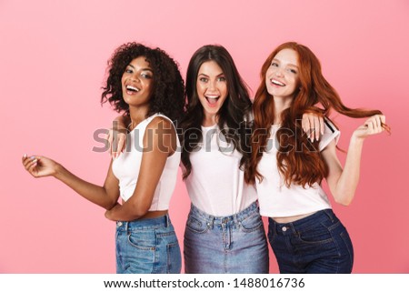 Photo of a positive smiling pleased young three multiethnic girls friends posing isolated over pink wall background.