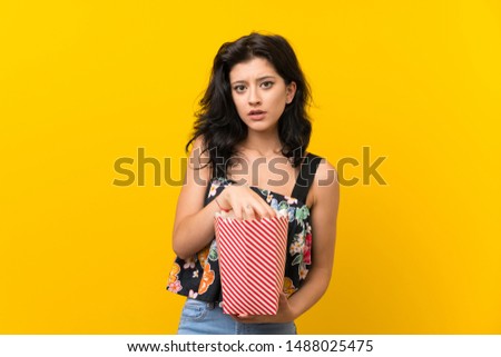 Young woman over isolated yellow background eating popcorns