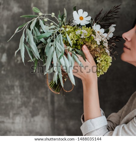 bouquet of white flowers in a glass jar in the hands of a girl florist on the background of a concrete wall. The concept of inspiration, congratulations, spring, decoration with flowers.