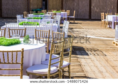 patio restaurant exterior decoration environment ready for some event wedding or birthday, wooden furniture chairs and table under white tablecloth 