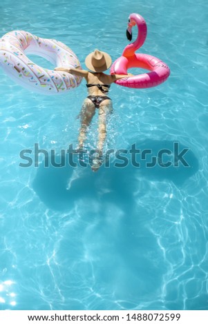 Woman in swimsuit and hat swimming with inflatable toys in the water pool, enjoying vacations during the summer time