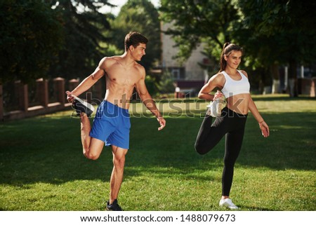 Guys have nice abs. Man and woman have fitness day in the city at daytime in the park.