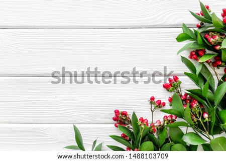 Green leaves and red berries frame on white wooden background top view copyspace