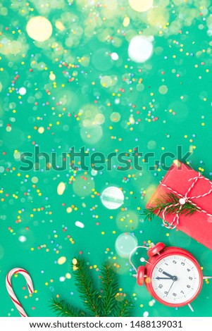 New Year or Christmas pattern flat lay top view with red alarm clock twelve midnight fir tree branch Xmas holiday celebration green paper bright colorful confetti background. Template text design 2020