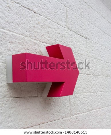 Pink arrow sign  hanging against white bricks wall for direction.