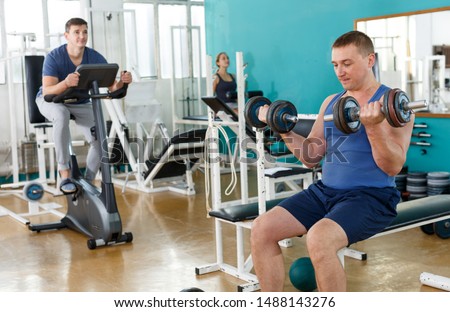 Portrait of man in sportswear lifting dumbbells at gym