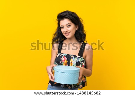 Young woman over isolated yellow background holding gift box