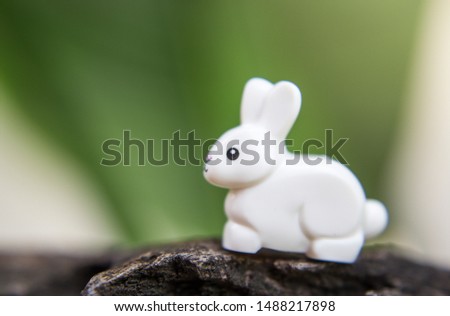 A white rabbit a toy on a stone among grass and flowers