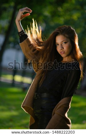 Portrait of young latin girl, posing with autumn / winter clothes, black dress, brown jacket, in the park.