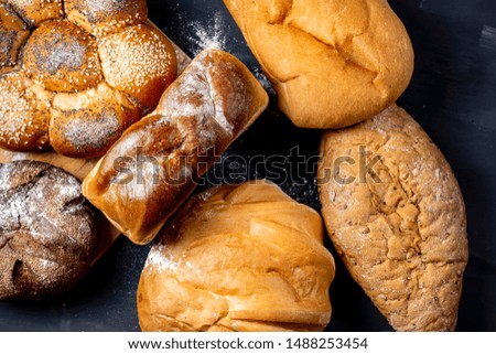 Assortment of freshly baked breads with ears of wheat on black background. Shallow depth of field.