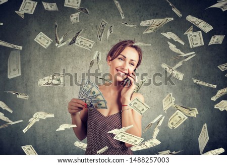 Excited attractive woman talking on a smartphone holding money, cashback under dollar rain 