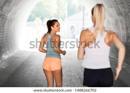 fitness, sport and healthy lifestyle concept - smiling young women or female friends with earphones running outdoors
