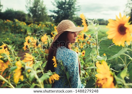 Young woman walks on blooming sunflower field. Happiness with nature. Beautiful woman posing in a field of sunflowers in a dress and hat at sunset. Summer holidays, vacation, relax and lifestyle.