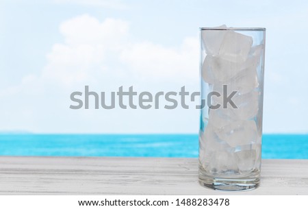 Refreshment glass of drink water with ice on white wood table with summer sea sky background.