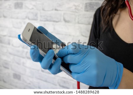 Young brunette woman student nurse/doctor using a  stethoscope checking the health of a smartphone with blue medial gloves on
