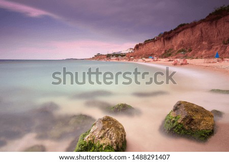 Seascape, stones in the foreground, on the right side of the photo beach with people and cliff