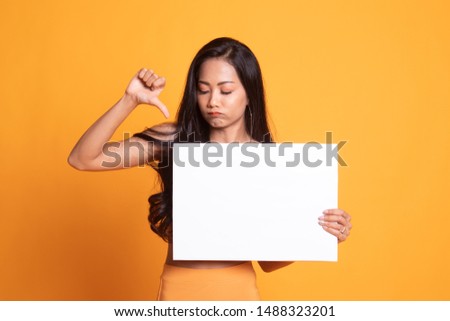 Young Asian woman show thumbs down with white blank sign on yellow background