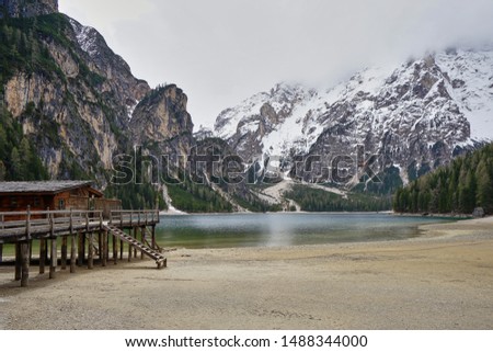 Landscape of Lake Pragser Wildsee / Lago di Braies, Dolomites, Italian Alps, Italy. Wooden hut, snowy mountain and fog. Taken in April in spring