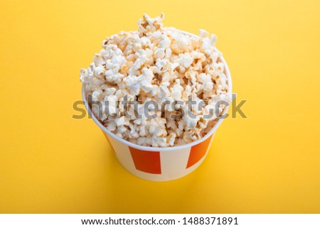 Striped paper cup with popcorn. Tasty popcorn on yellow background. Snack for a movie, an idea for a meal. Close-up, top view. Copy space for text.