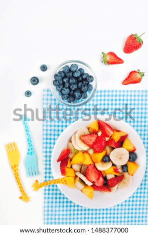Fruit salad on the white plate served for kids with funny giraffe forks on white background with blank space for text. Top view, flat lay.
