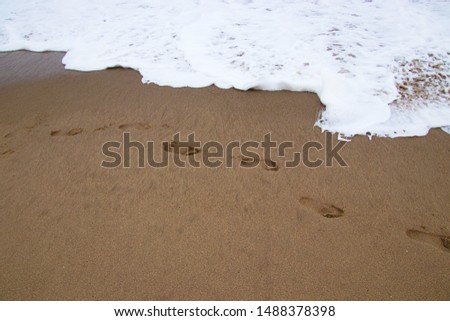 Footprints in the sand at the edge of a coming wave