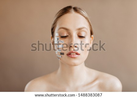 Sad girl with words written on her face crying with closed eyes on beige background