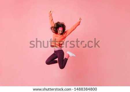 Lovely brunette girl in pink sports headband and tracksuit jumps on isolated pink background Royalty-Free Stock Photo #1488384800