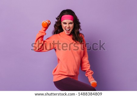 Active woman in sports bright outfit emotionally demonstrates exercises for hands with dumbbells Royalty-Free Stock Photo #1488384809