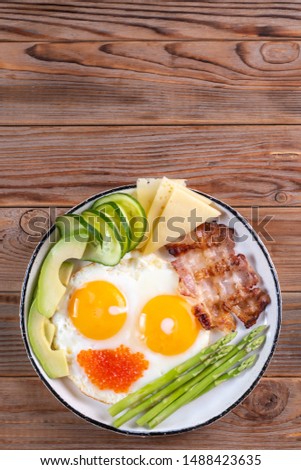 Top vertical view of ketogenic diet breakfast on the white plate on wooden background with copy space Royalty-Free Stock Photo #1488423635
