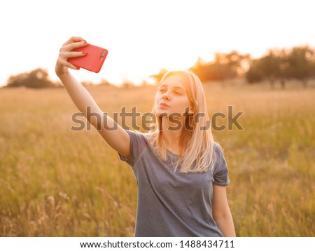 Young woman making selfie on the field at sunset