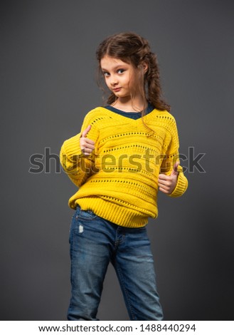 Beaitiful kid girl posing in fashion blue jeans and yellow pullover on grey studio background