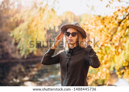 portrait of a blonde in sunglasses on a background of autumn nature. the frame is lit by sunlight. A young woman in a gray hat looks at the autumn forest.