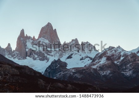 View of Snowcapped peaks of Cerro Torre, Laguna Torre hiking trek. Red bush tree foreground in autumn fall. Mountains, nature, travel. Blue sky. Shot in El Chalten, Mount Fitzroy, Patagonia, Argentina