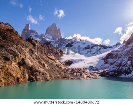 Mount Fitzroy aerial DRONE view. Patagonia trek. Scenic snow capped mountains. Blue sky background with turquoise lake and scenic rock landscape. Shot in Argentina. Nature, travel, adventure, hiking.