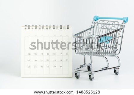 High season holiday shopping, black friday or monthly special offer concept, miniature small shopping cart or trolley with white clean desktop calendar on white background.