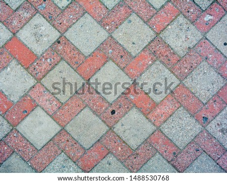 Red and gray road tiles on city street pavement with growing moss in mortar. Road construction background. Cobblestone pathway paved with grey and red decorative bricks. Road cover surface texture