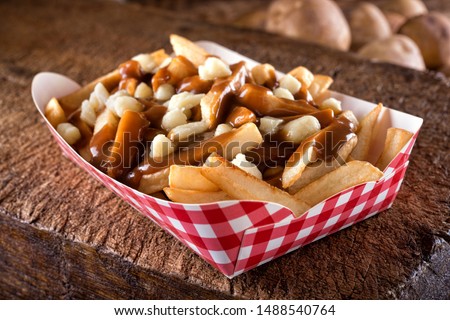 A serving of delicious poutine with french fries, cheese curds and gravy on a rustic wooden board. Royalty-Free Stock Photo #1488540764