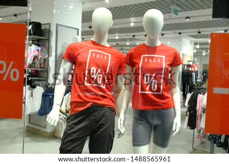 Window of Boutique With Two Mannequins in T-Shirts With Signs Advertising Sale for Sport Clothes at Shopping Center.
