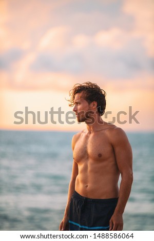Beach body muscular man with six pack abs handsome good looking guy enjoying relaxing on summer Hawaii vacation sunset. Surfer lifestyle.