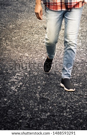 Partial view of stylish female legs in jeans and black sneakers on the road