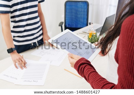 Block scheme on screen of tablet computer in hands of teenage girl talking to classmate and dicussing project