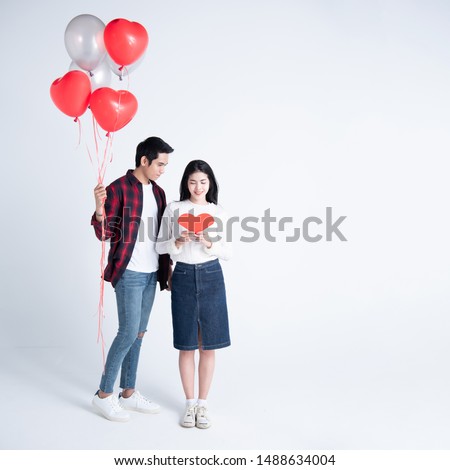 Beautiful young couple at home. Hugging, kissing and enjoying spending time together while celebrating Saint Valentine's Day with gift box in hand and air balloons in shape of heart on the background