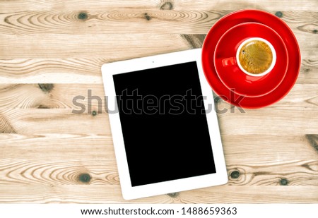 Digital tablet with black screen and red cup of coffee on wooden table. Flat lay