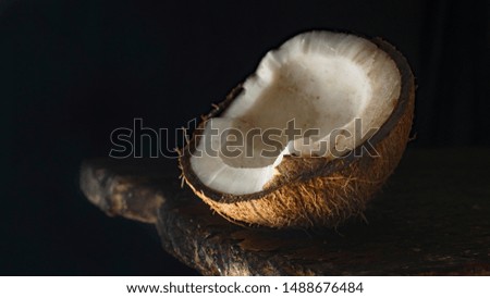 Close-up of half ripe coconut on rough wood, black background