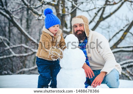 Father and son making snowman. Dad and baby son playing together outdoors. Happy father and son - winter portrait