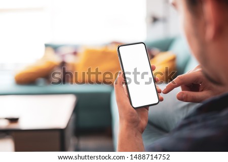 Man using smartphone frameless mockup blank screen in home interior Royalty-Free Stock Photo #1488714752