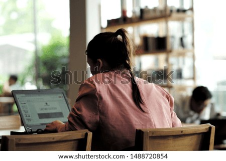 Back portrait of woman works hard on her laptop with defocused customers at the coffee shop. Office syndrome concept. Lifestyle of people working at co working space.