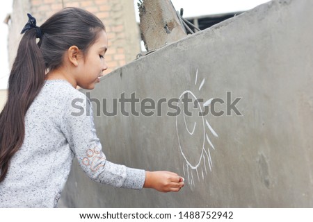 Little latin girl drawing sun on the wall.