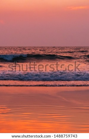 scenic view of natural lighting after sunset at the beach, vertical picture with ocean waves and orange and pink sky. shimmering wet sand reflecting natural warm sunlight at cavelossim, goa, india.