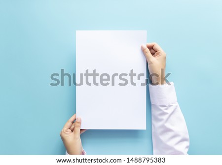 close up hands holding  empty white blank letter paper size A4 for flyer or invitation mock up isolated on a blue background.